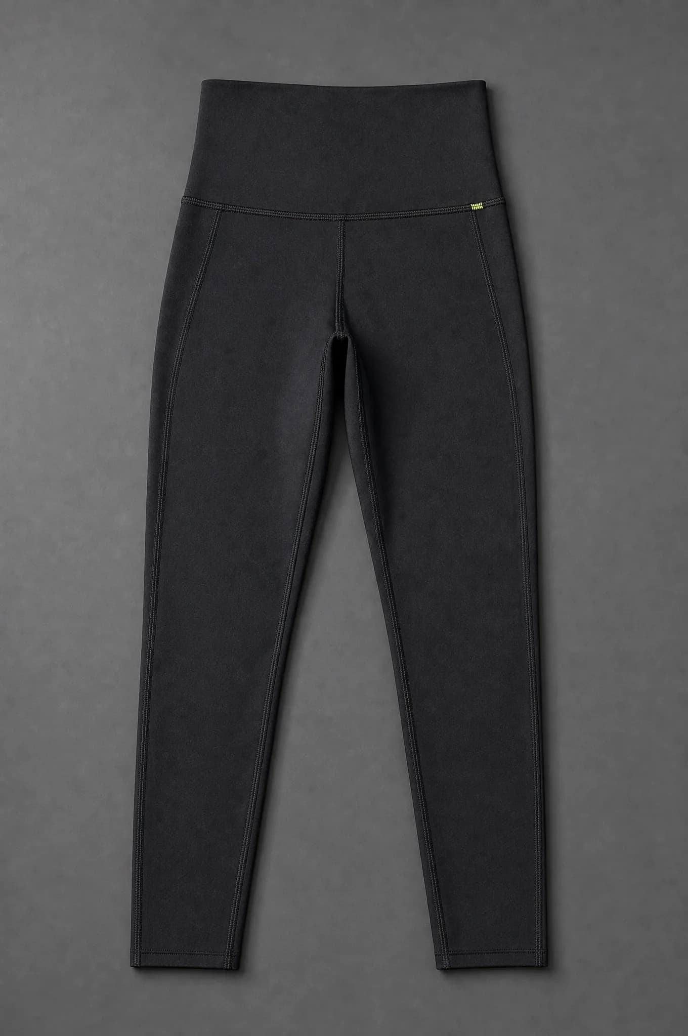 A pair of black high-waisted leggings photographed flat from above, empty and unworn, showing a wide waistband and flatlock seams.